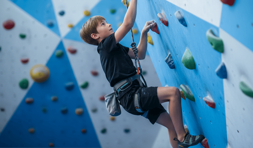 A young boy climbing up a wall in a rock climbing gym