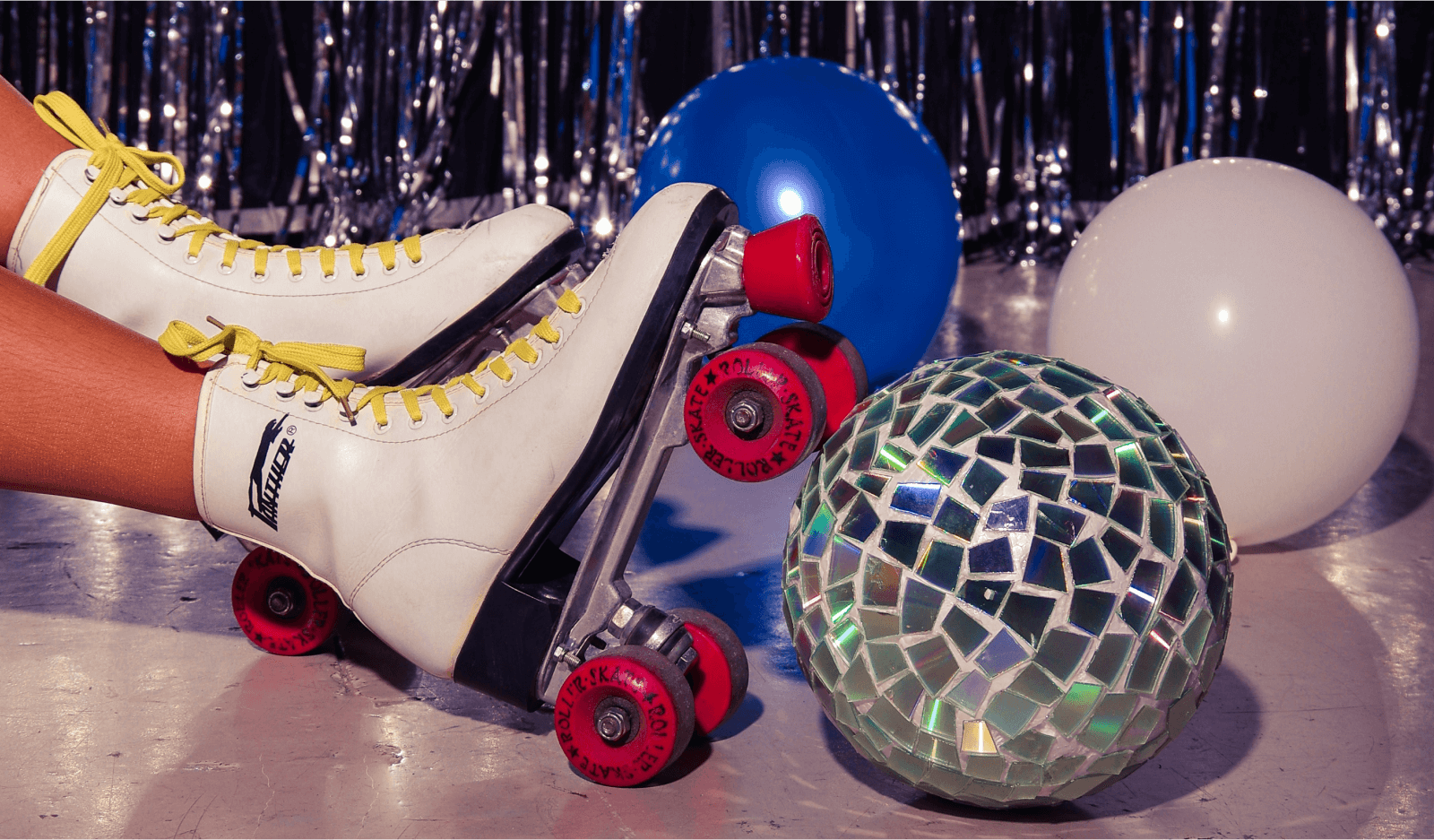 A retro roller skate next to balloons and a disco ball