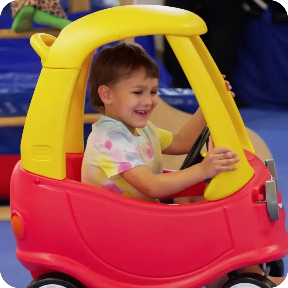 Toddler behind the wheel of a ride-on toy car in the play area